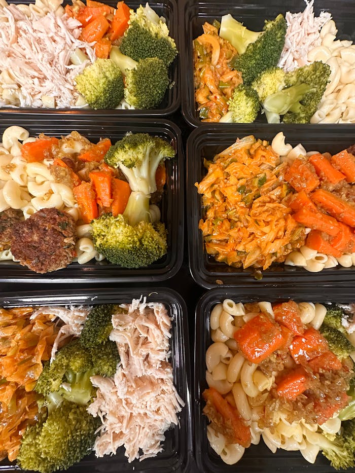services-05 Colorful meal prep trays with pasta, broccoli, shredded chicken, and carrots, ready for healthy eating.